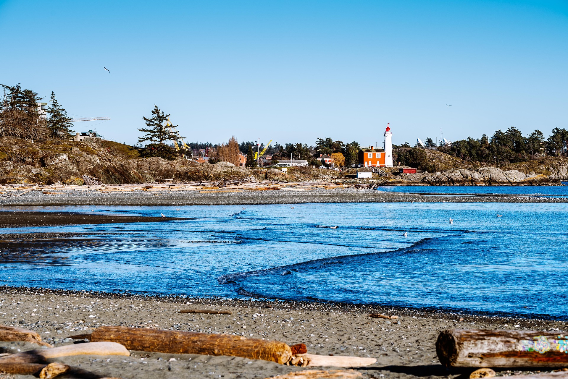 Pebble beach and shoreline with structures and a lighthouse in the distance