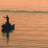 Silhouette of a person fishing on a boat at sunset