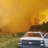 A BC government truck and wildfire personnel on a road with a wall of smoke and fire in the background